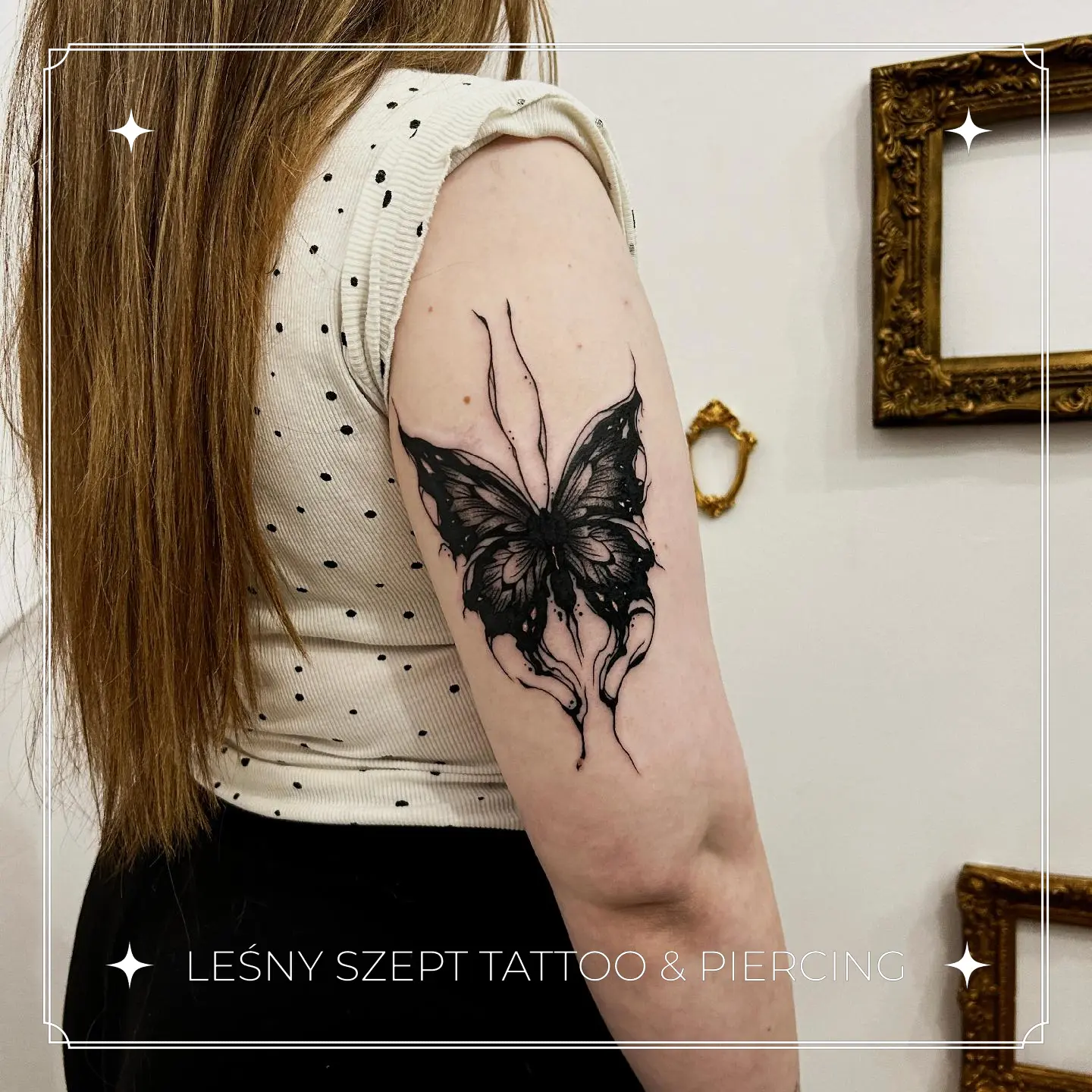 Czarny tatuaż motyla z dymnymi, abstrakcyjnymi skrzydłami na ramieniu