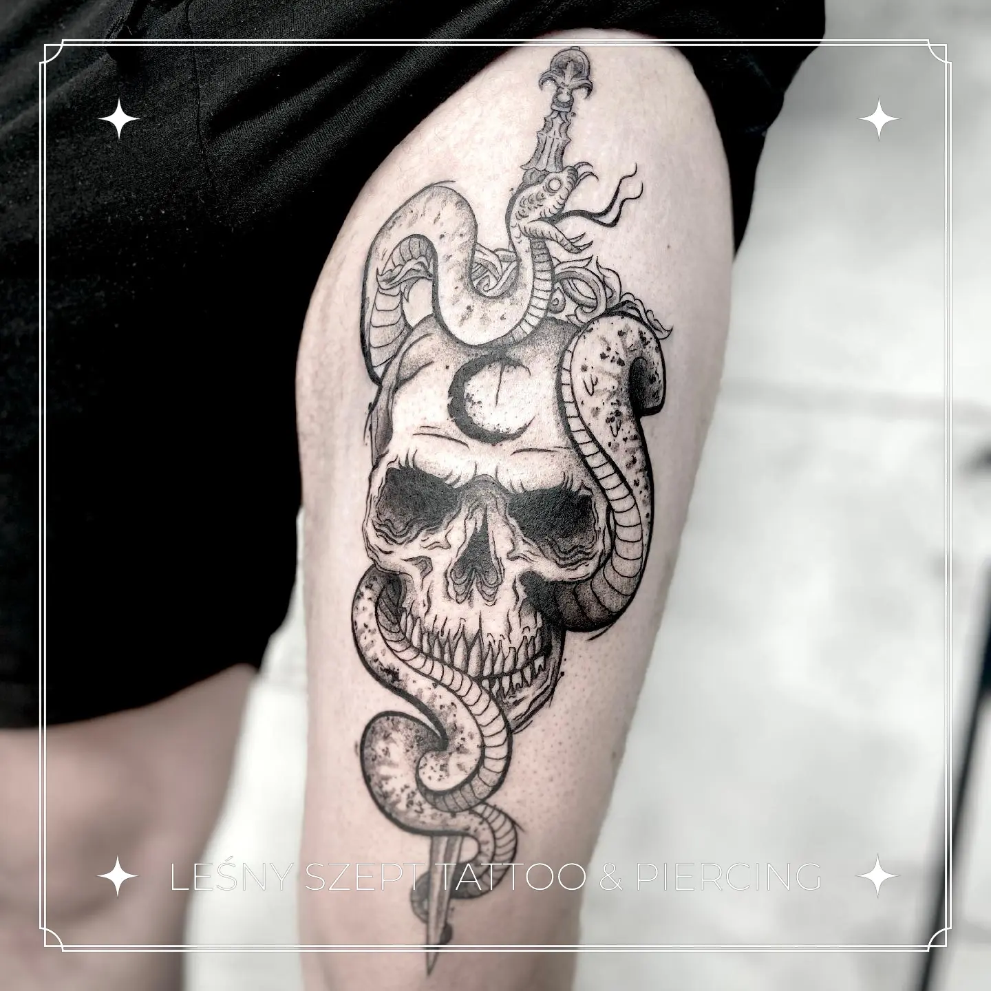 Tatuaż czaszki z sierpem księżyca, oplecionej przez dwa węże i sztylet, na udzie