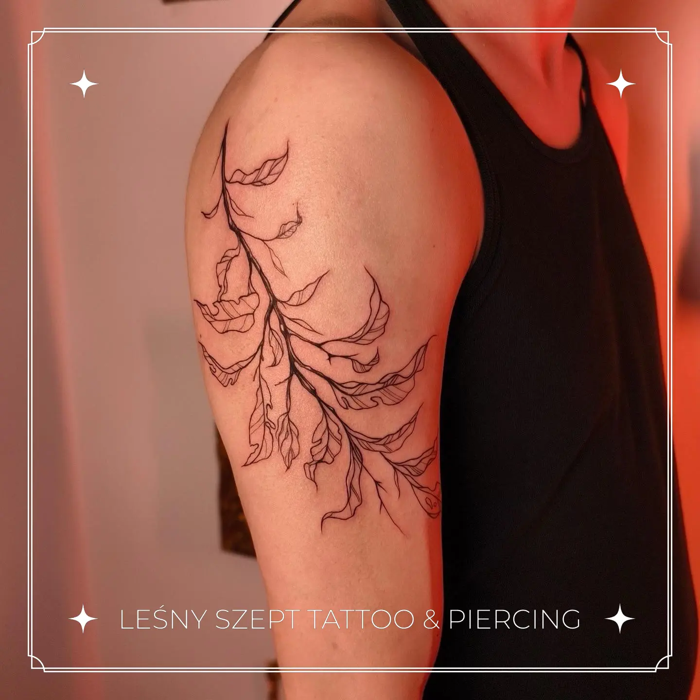 Tatuaż delikatnej gałęzi z falującymi liśćmi na ramieniu