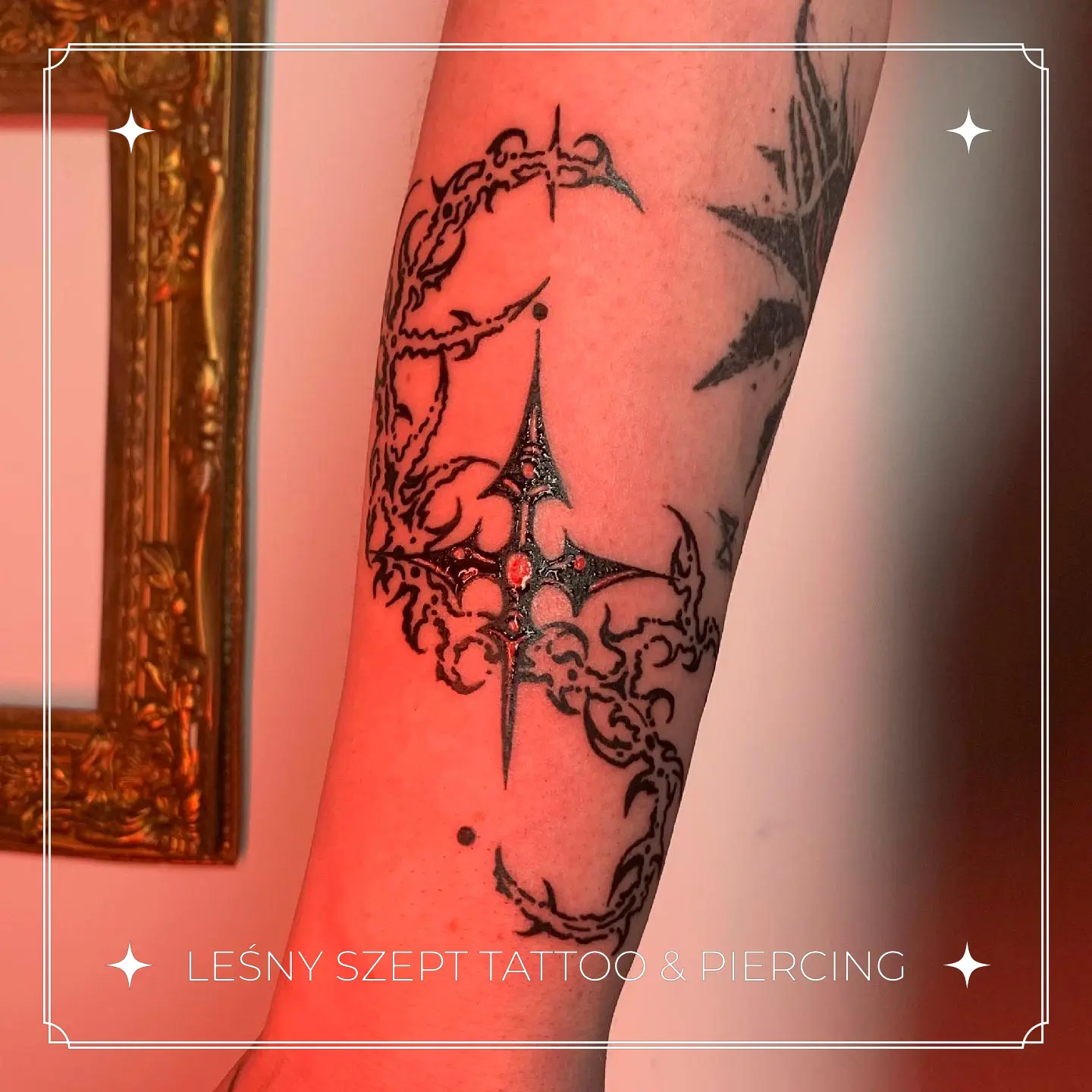Tatuaż gotyckiego ornamentalnego krzyża z czerwonymi kamieniami na przedramieniu